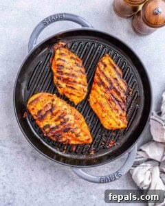 Chicken breasts cooking on a stovetop grill pan with dark sear marks forming.