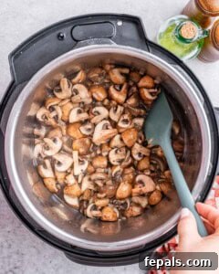 Sautéed mushrooms and onions being stirred with a spatula inside the Instant Pot.
