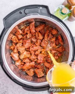 Pouring beef broth into the Instant Pot over seasoned beef chunks.