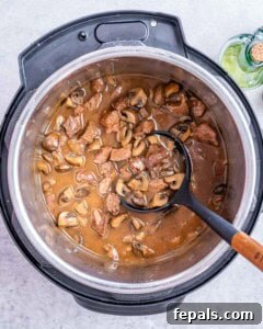 Rich mushroom sauce simmering eith beef in the Instant Pot with a ladle resting inside.