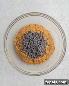 Chocolate chips being added to the sweet potato batter in a bowl.