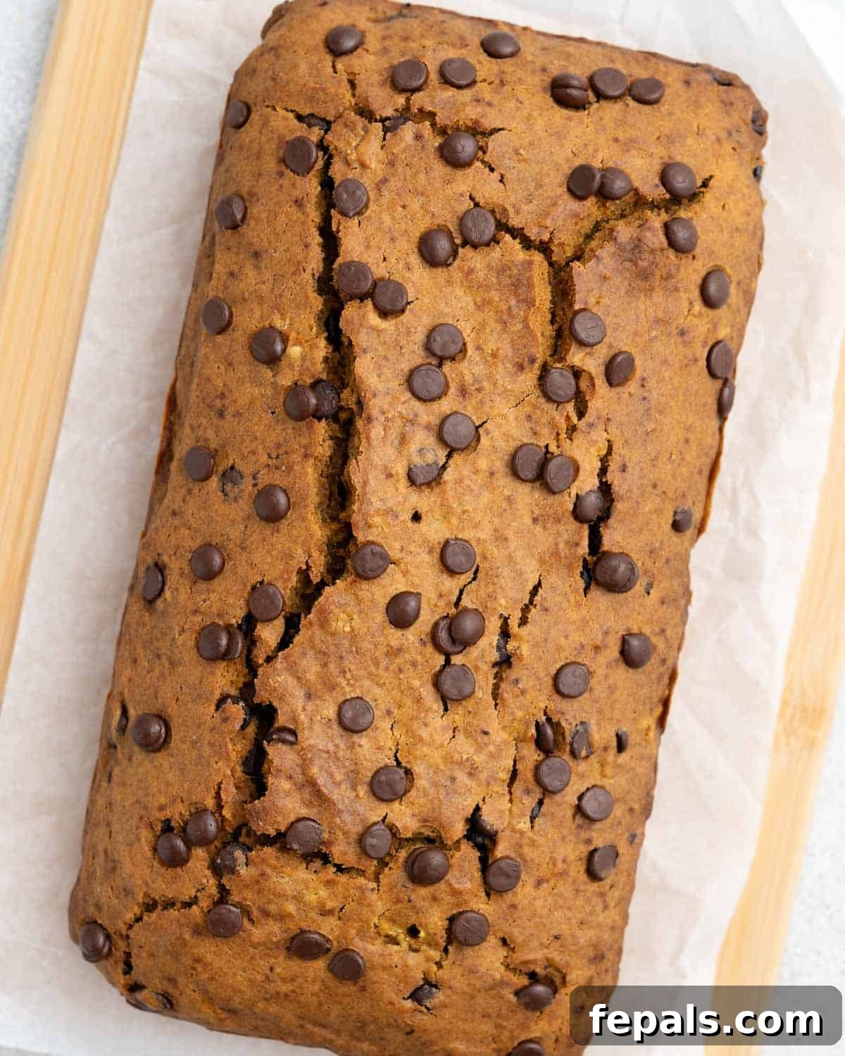 A beautiful whole sweet potato bread loaf, glistening with a golden-brown crust, resting on a rustic cutting board, ready to be sliced.