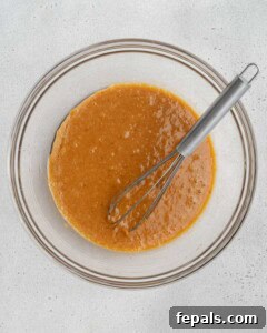 Wet batter made of oil, egg, sugar, and sweet potatoes mixed in a bowl.