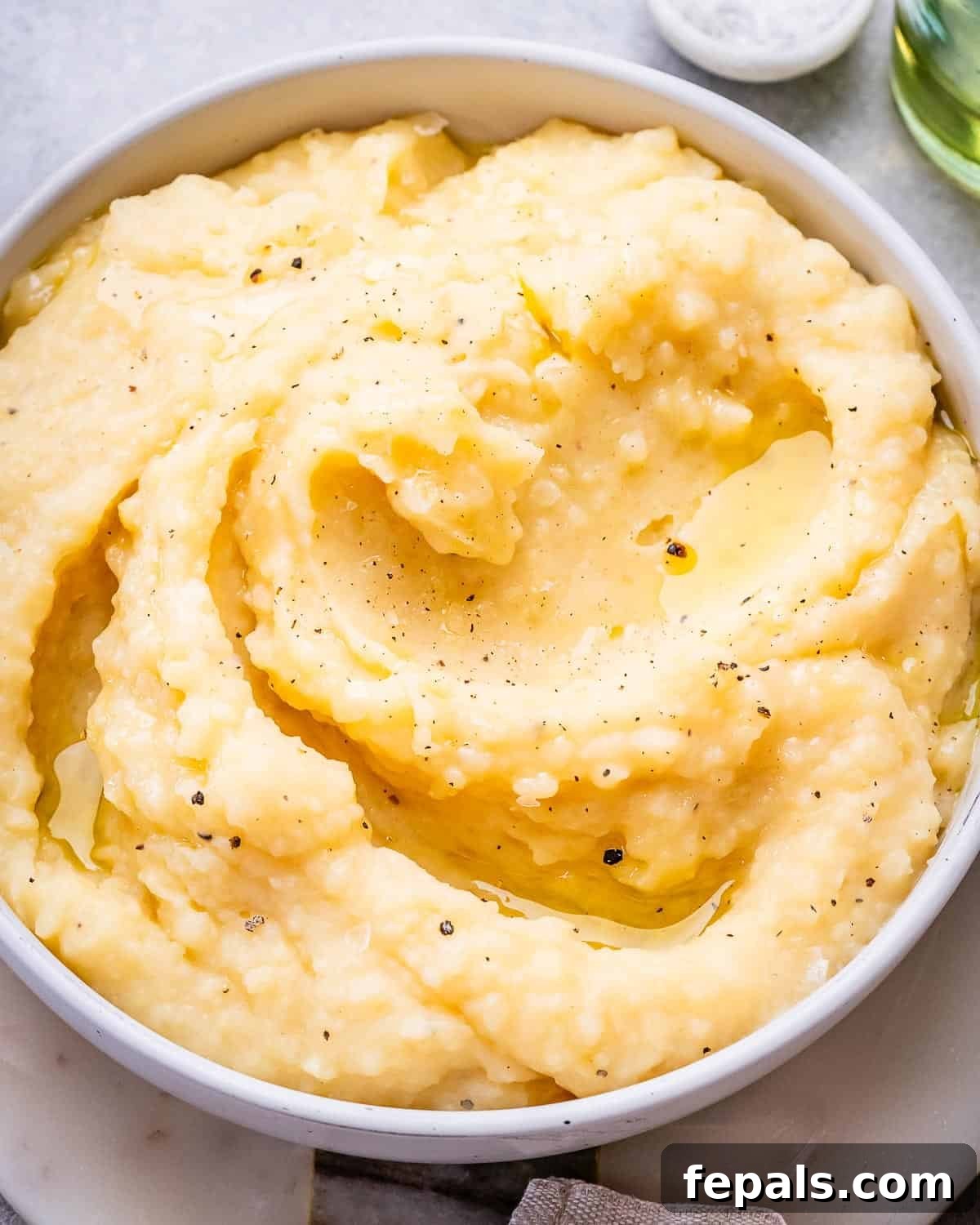 A serving of fluffy mashed potatoes in a bowl, generously seasoned with fresh black pepper and drizzled with melted butter for a rich finish.