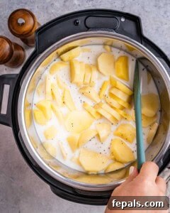 Instant Pot filled with sliced golden potatoes being stirred with a spatula before cooking.