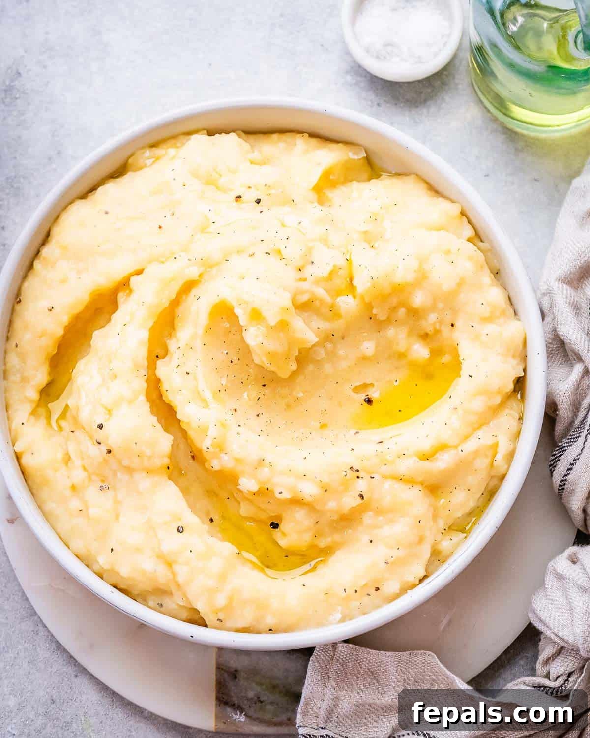 A stunning close-up of smooth, golden mashed potatoes presented in an elegant serving bowl, with exquisite swirls of melted butter and a garnish for aesthetic appeal.