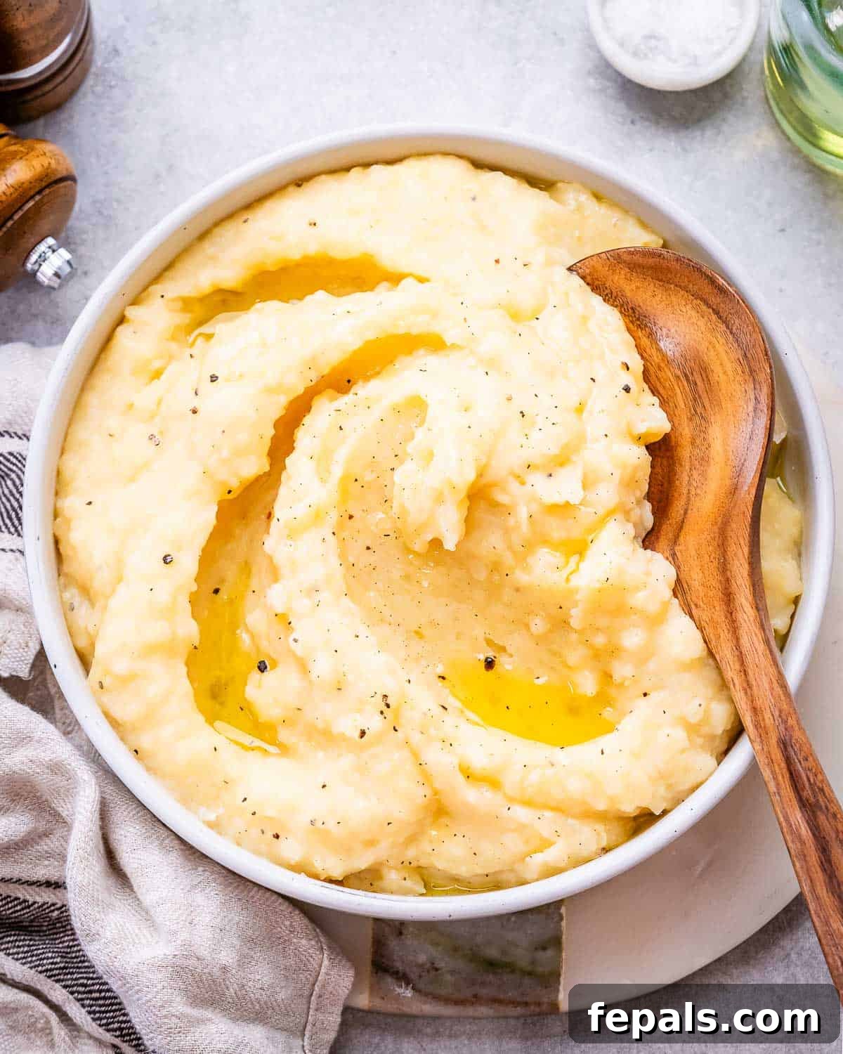 A close-up of smooth, golden mashed potatoes in a white serving dish, adorned with rich swirls of melted butter, inviting to taste.