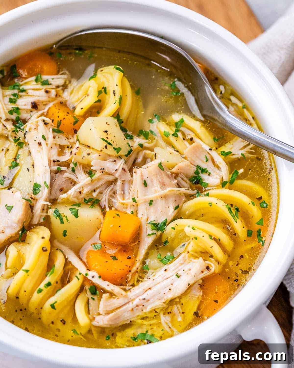 Overhead view of a steaming bowl of chicken noodle soup, garnished with fresh parsley and filled with hearty vegetables.