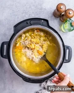 Instant Pot filled with hot broth and noodles being stirred with a ladle.