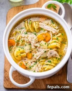 A white bowl filled with homemade Instant Pot chicken noodle soup, loaded with carrots, potatoes, and rotini noodles.