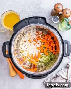 Diced onion, celery, and carrots being sautéed inside the Instant Pot with broth nearby.
