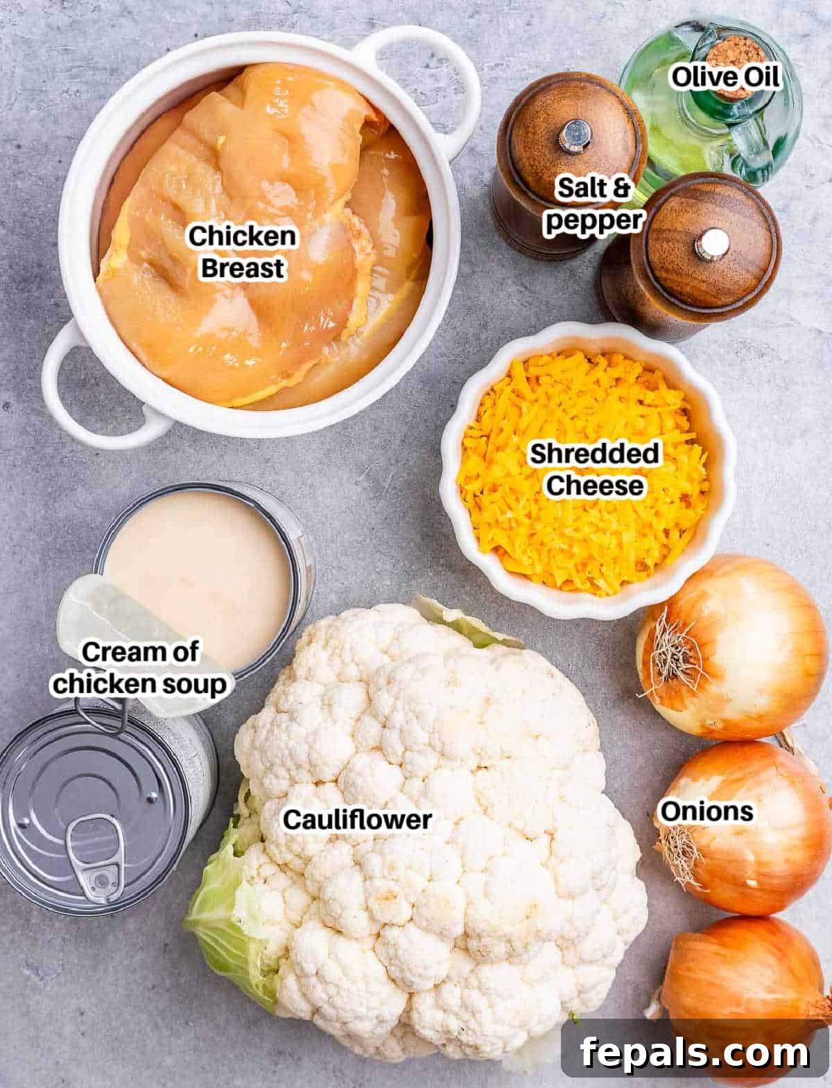 A selection of fresh ingredients including yellow onions, chicken breast, cauliflower, and cheese, laid out for French onion chicken casserole preparation.