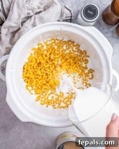Adding uncooked pasta and liquid ingredients to the slow cooker for mac and cheese.