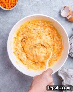 Mixing bowl with grated carrots and golden being stirred together with a wooden spoon.