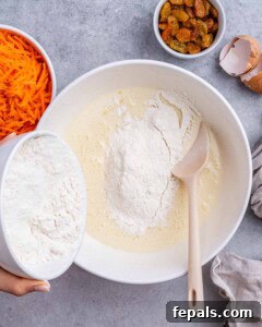 Flour being added into the wet ingredients in a mixing bowl with a wooden spoon.