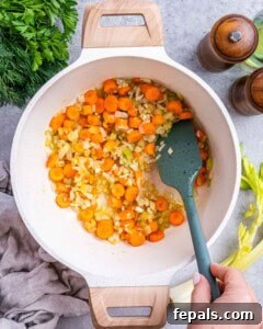 Avgolemono Soup: A Bowl of Bright Comfort 9 Chopped carrots, celery, onions, and garlic being sautéed in a pot with a spatula.