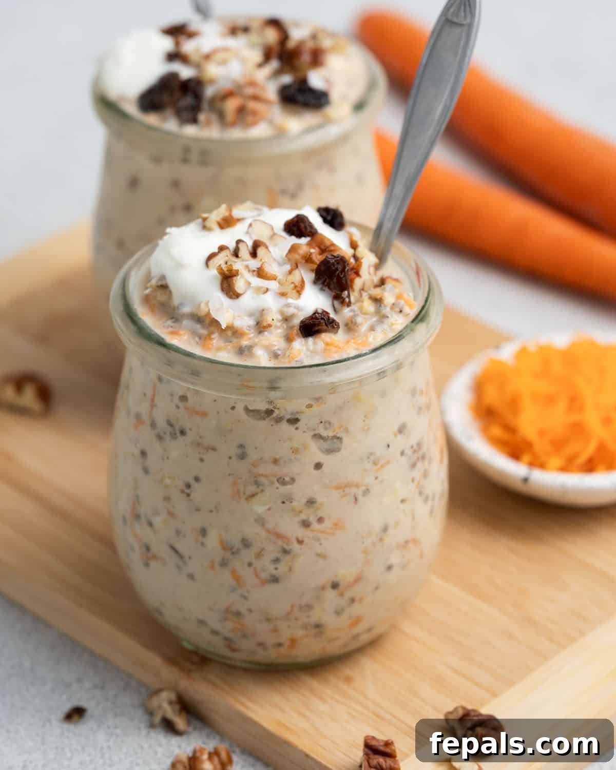 Spiced Carrot Cake Overnight Oats 2 A jar of carrot cake overnight oats with a spoon on a wooden board, ready to be enjoyed.