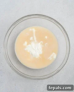 Mixing almond milk, Greek yogurt, vanilla extract, and maple syrup in a bowl.