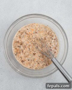 A bowl of carrot cake overnight oats mixture after initial stirring, showing combined ingredients.