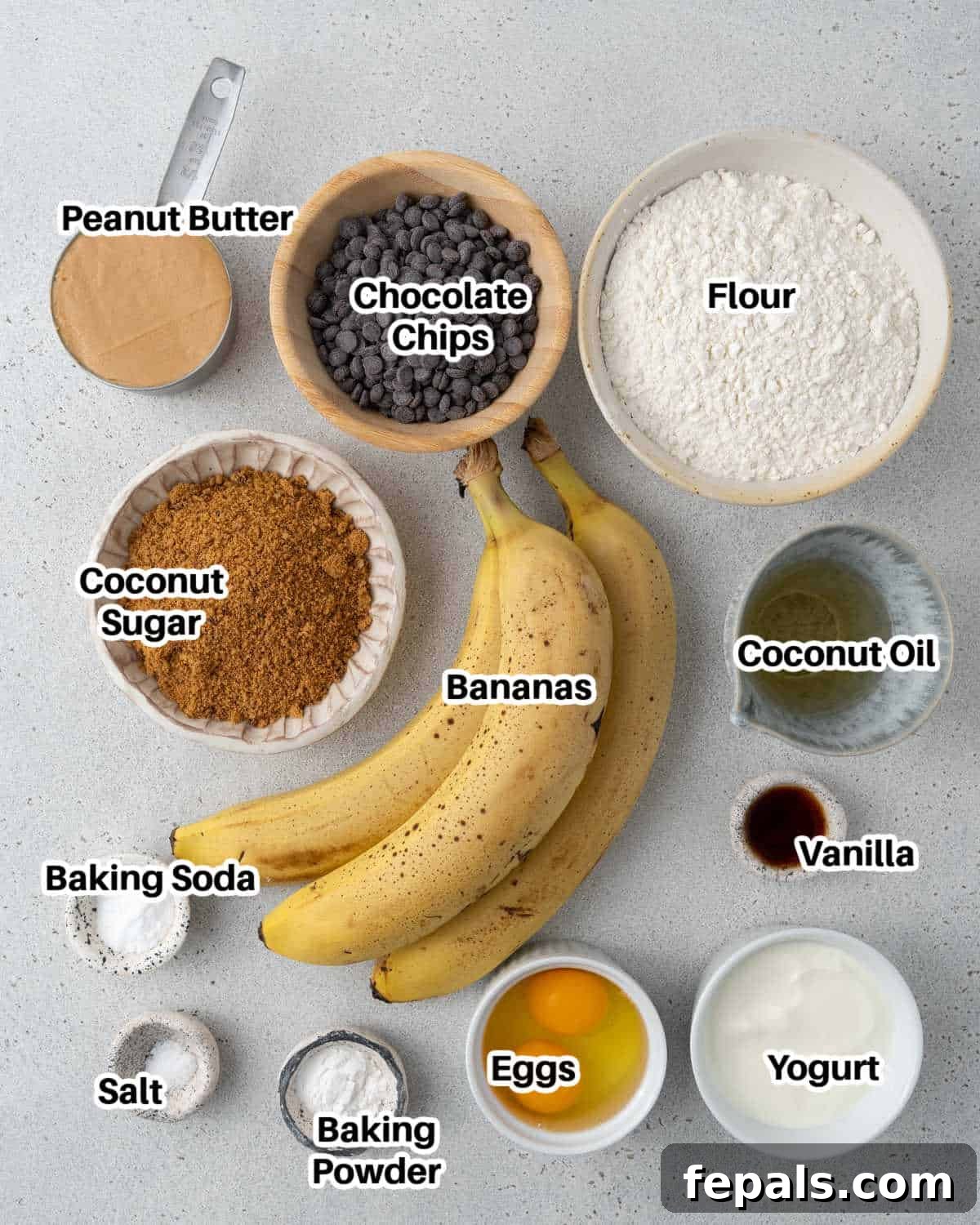 Various ingredients laid out for making peanut butter banana bread, including ripe bananas, flour, eggs, and chocolate chips.