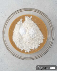 flour added over the wet mixture in a bowl for banana bread.