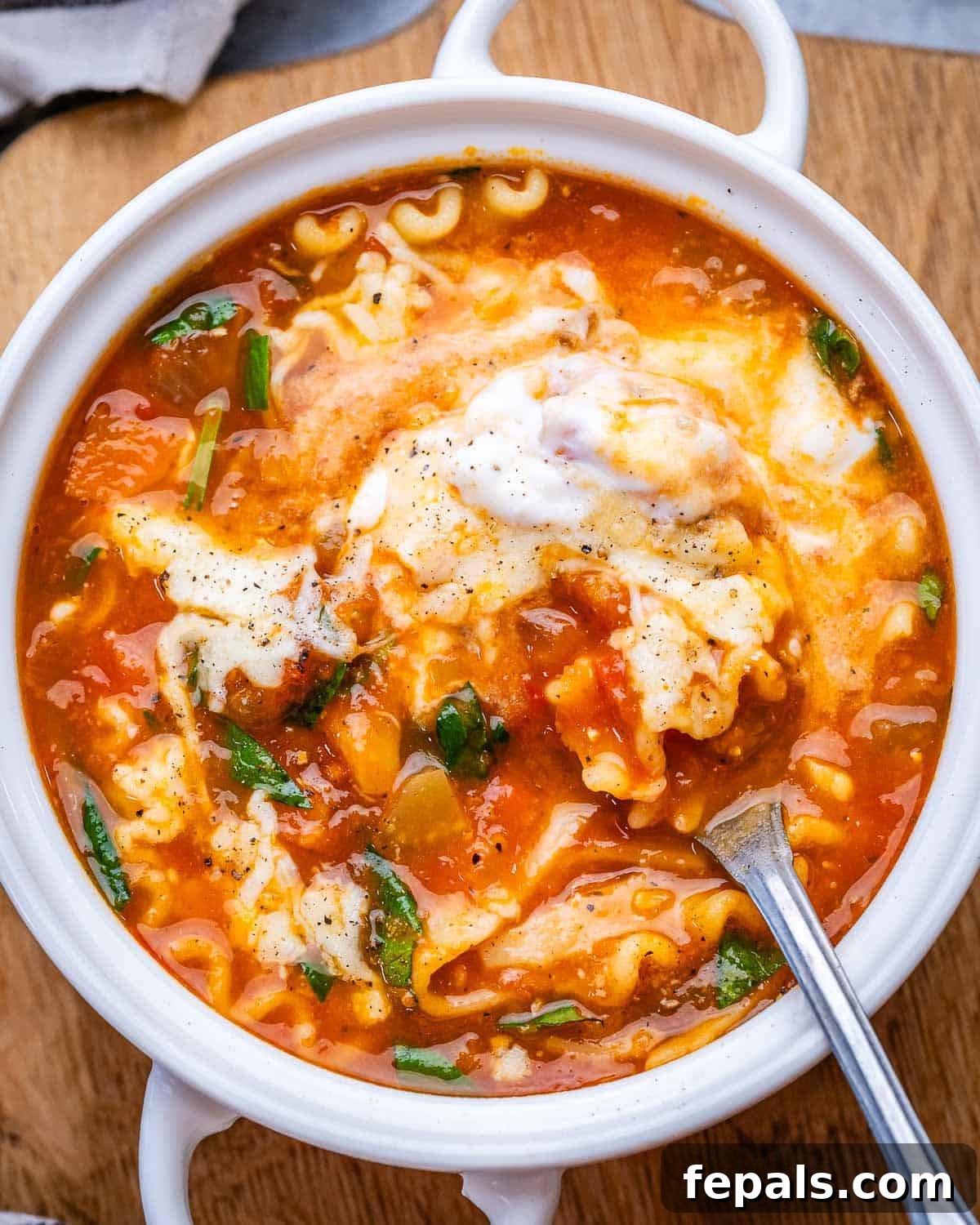 A white bowl of vegetarian lasagna soup topped with mozzarella and parmesan cheese and fresh basil.
