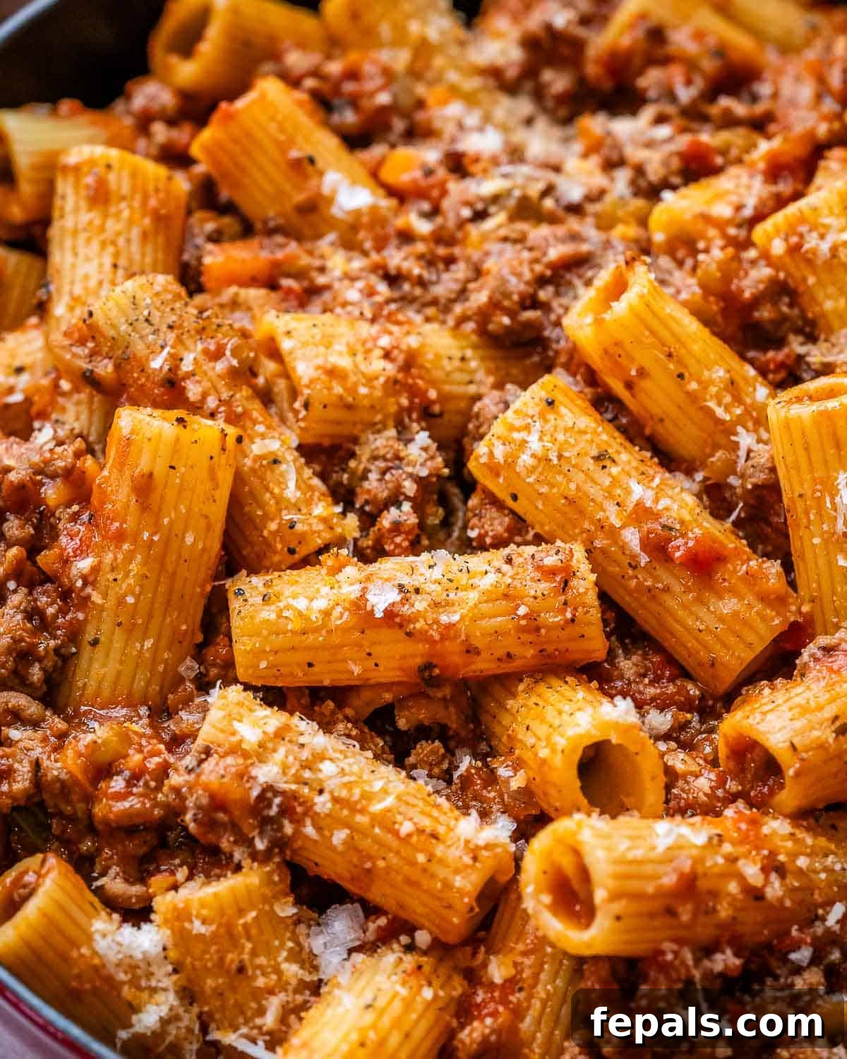 A close-up of rigatoni bolognese in a skillet, showcasing the rich sauce and pasta texture.