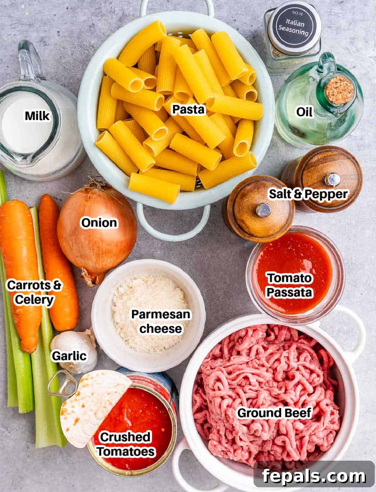 A selection of fresh ingredients laid out for making rigatoni bolognese, including vegetables, ground beef, and pasta.