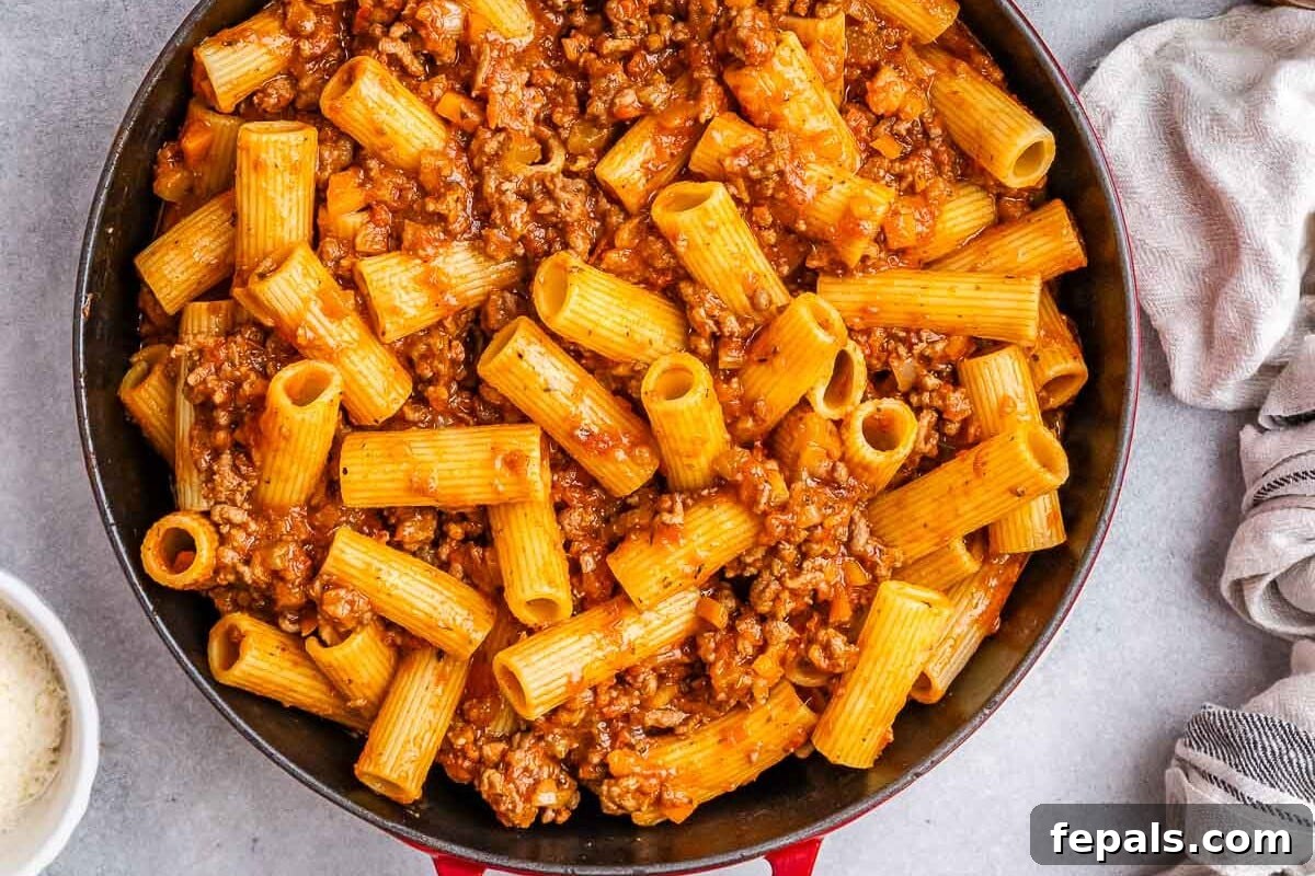 A vibrant red skillet filled with rigatoni pasta generously coated in a rich meat sauce.