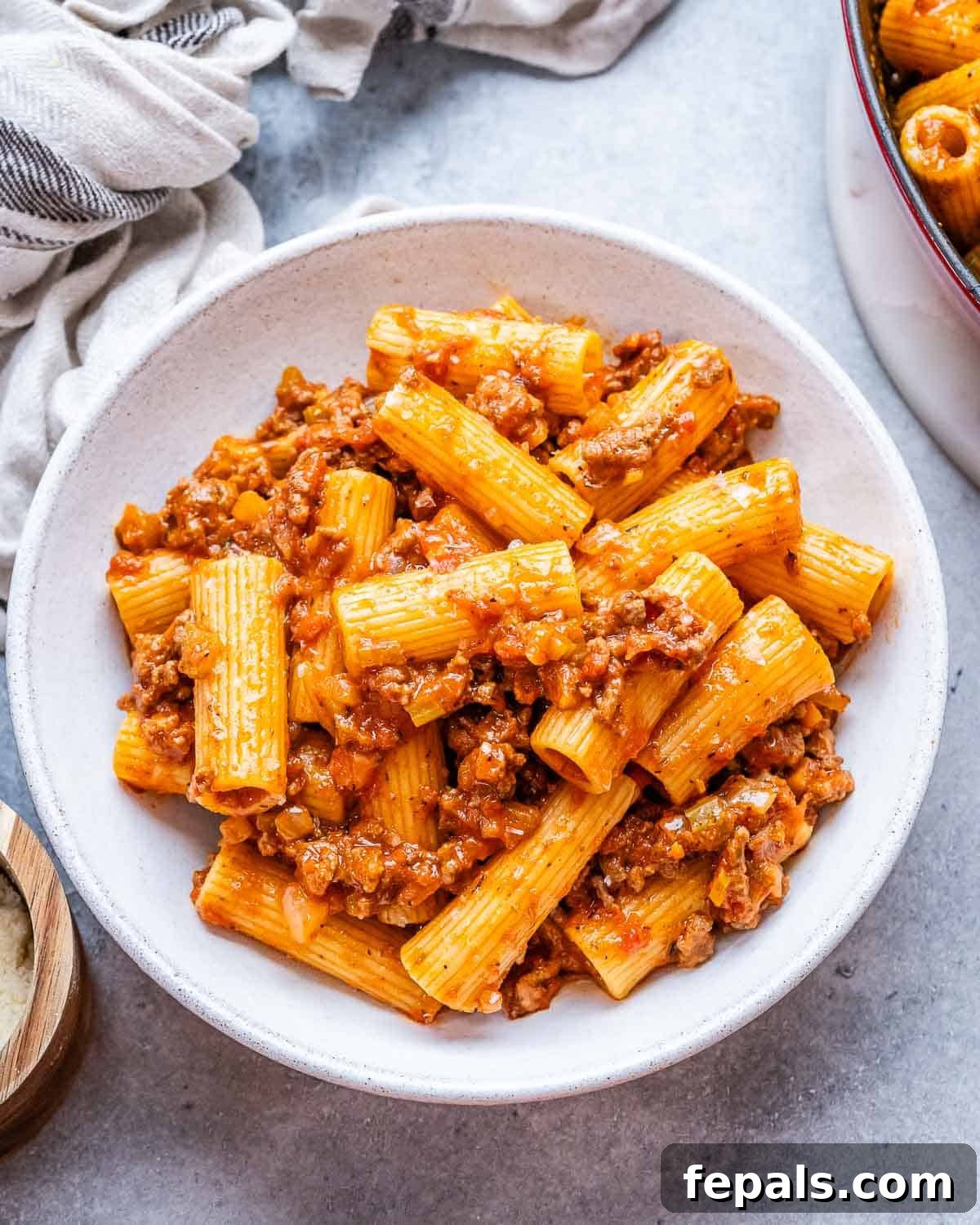 A white bowl showcasing a generous serving of Rigatoni Bolognese, garnished with fresh herbs.