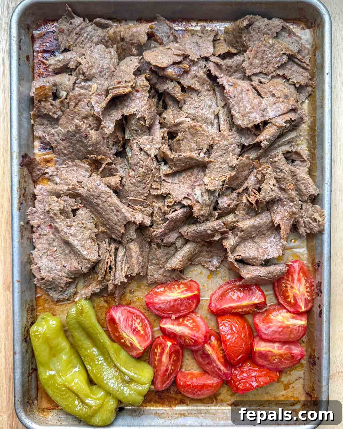 Shredded doner kebab piled high on a sheet pan, surrounded by roasted tomatoes and peppers, ready to be served with fresh ingredients.