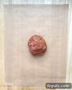 Meat mixture being rolled out thinly on parchment paper.