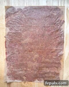 The meat sheet being rolled into a log with the parchment paper.