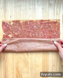 Rolled doner kebab meat logs placed on a baking sheet with peppers and tomatoes.