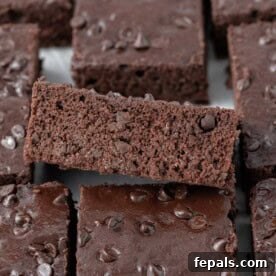 A perfectly stacked pile of sliced Greek yogurt brownies, revealing a moist, fudgy interior studded with melted chocolate chips on top, promising a decadent yet healthier dessert.