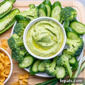 Top view of a vibrant green dip made with creamy avocado and tangy Greek yogurt, artfully surrounded by crisp slices of cucumbers and fresh broccoli florets, perfect for healthy snacking.