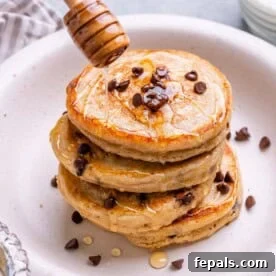 Side angle of Greek yogurt pancakes with honey being drizzled from a dipper, showcasing their golden-brown perfection and enticing texture.