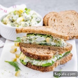 Side shot of a perfectly prepared egg salad sandwich, sliced in half and presented on a clean white plate, emphasizing its fresh ingredients and inviting texture.