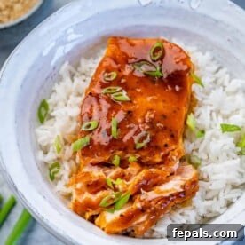 Flaked baked honey salmon over white rice in a white bowl garnished with sliced green onions