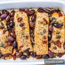 Top view of baked salmon fillets in a white baking dish topped with olives and capers