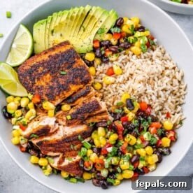 A bowl with brown rice, southwest bean salad, salmon, sliced avocado, salmon, and lemon slice.