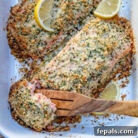 A wooden spoon grabbing a piece of baked salmon crusted with Parmesan from a dish.