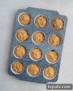 batter adding into muffin cups in a pan.