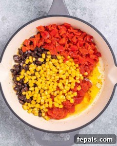 Overhead shot of diced tomatoes, corn, and black beans in a skillet with olive oil.