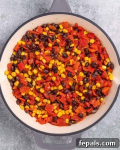 Skillet filled with black beans, corn, and roasted red peppers being cooked together.
