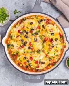Top view of freshly baked Santa Fe chicken skillet with melted cheese, beans, corn, and colorful veggie toppings.