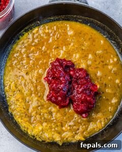 Adding cranberry sauce to an orange sauce in a pan.
