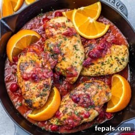top view of a black skillet that has 4 cooked chicken breasts in an orange cranberry sauce with orange slice garnishes around the chicken