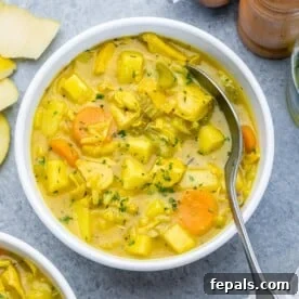 Spiced Anglo-Indian Mulligatawny 8 a round bowl of soup with chicken and veggies that's yellow in color.