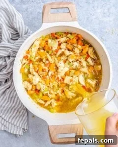Pouring chicken stock into the pot with chicken, pasta, and vegetables, then stirring in balsamic vinegar.